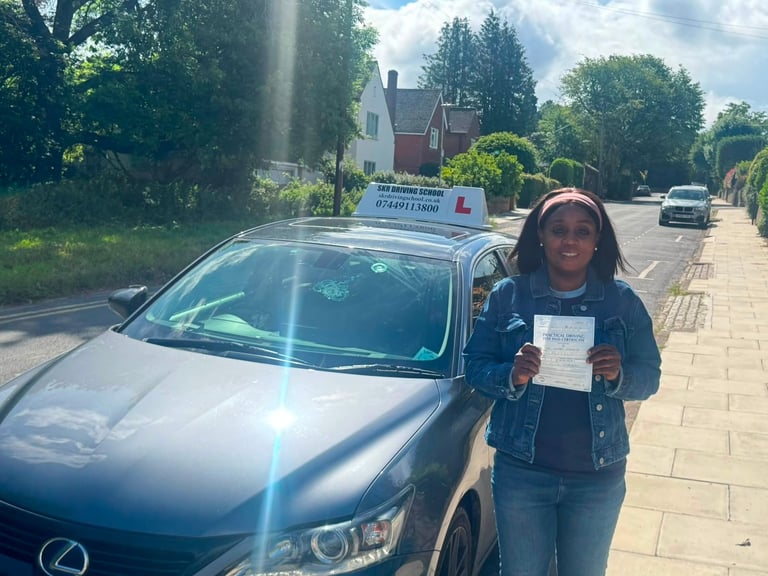 Woman holding certificate standing next to silver car on suburban street with brick pavement